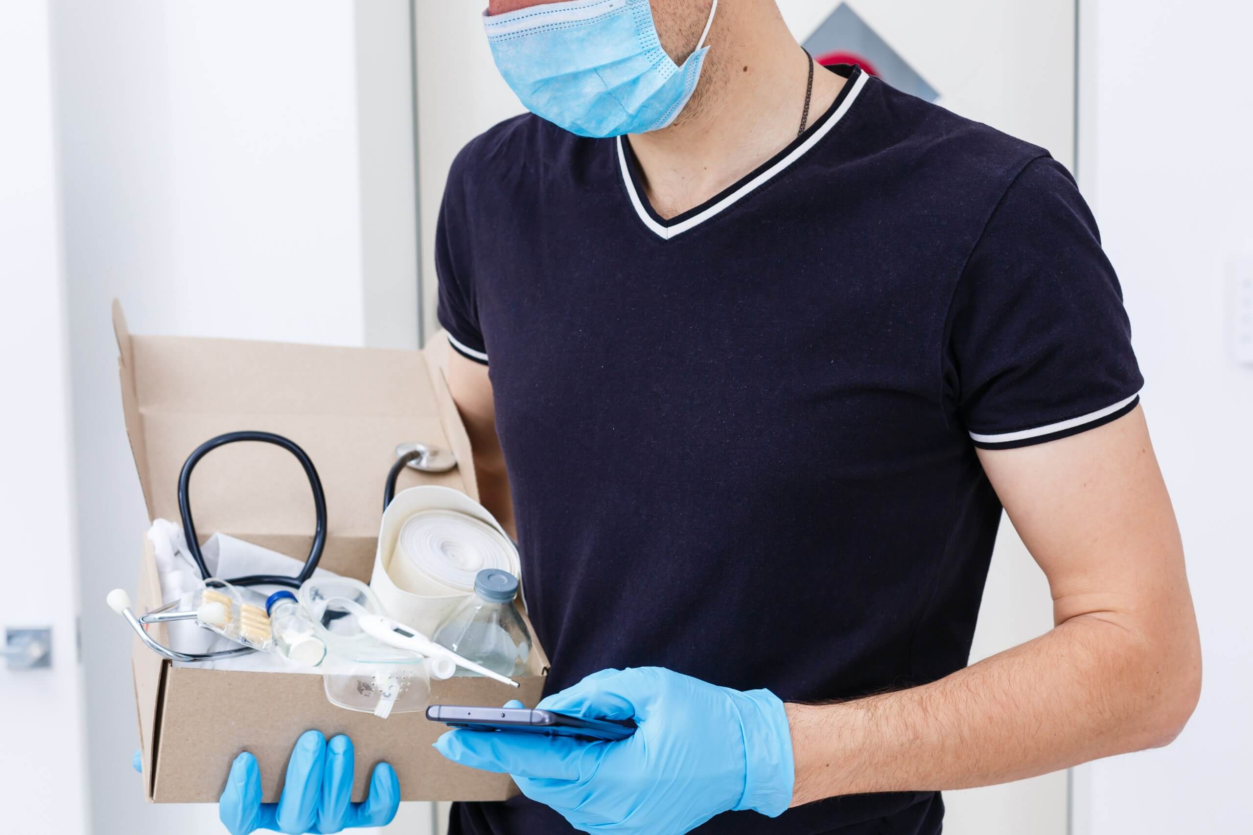 Man with face mask and vinyl gloves holding a box with medical supplies